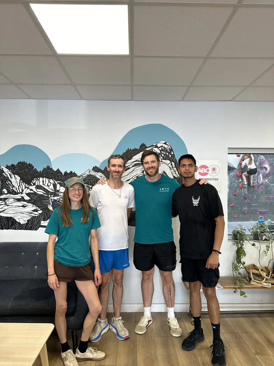 Four people standing in front of a mountain mural at a climbing wall, one wearing a black YAKA tee